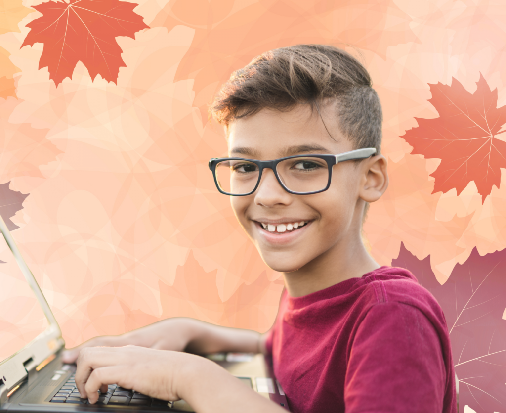 Smiling student wearing glasses working on a laptop, with autumn leaves behind